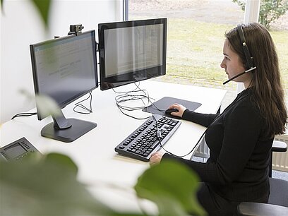 Eine junge Frau mit Headset arbeitet am Computer.