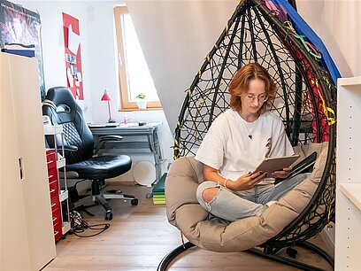 Eine Jugendliche sitzt in einem Hängestuhl und arbeitet an einem Tablet. 