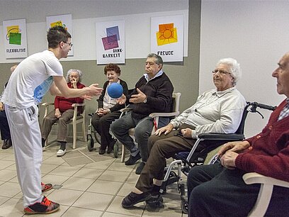 Eine Frau macht Bewegungsübungen mit einer Gruppe von älteren Menschen in einem Pflegeheim.