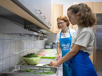 Zwei Frauen schneiden Bohnen in einer Küche zu.