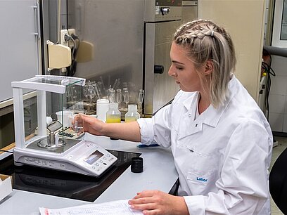 Eine junge Frau sitzt im Labor an einem Tisch und verschließt eine Probenanwendung.