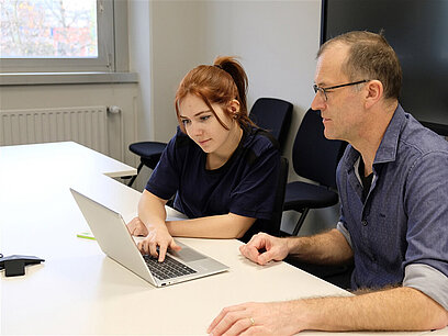 Eine junge Frau und ein Mann schauen sich gemeinsam etwas auf einem Laptop an.