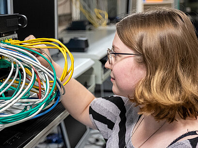 Ein Mädchen schaut auf verschiedene Kabel an der Rückwand von einem Gerät.