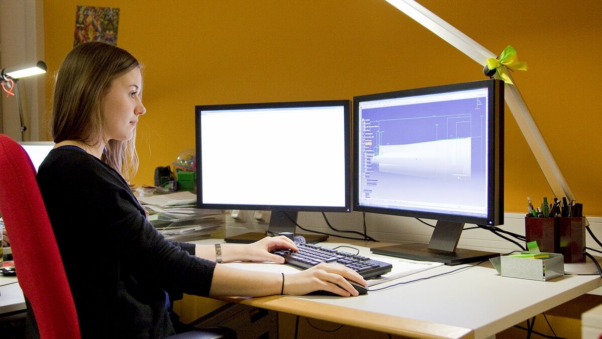 Eine junge Frau sitzt am Schreibtisch vor zwei Bildschirmen.