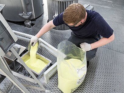 Ein junger Mann mit Handschuhen füllt Kunststoffgranulat in eine Maschine.