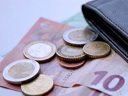Münzen und Geldscheine liegen neben einem Geldbeutel.