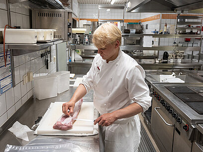 Ein Koch schneidet mit einem Messer ein Stück Fleisch zurecht. 