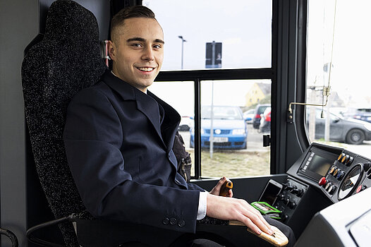 Ein junger Mann sitzt im Fahrerstand eines Linienbusses.