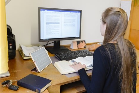 Ein Mädchen sitzt mit einem aufgeschlagenen Buch vor dem Computer.