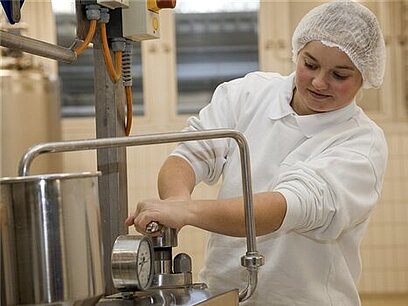 Eine Milchtechnologin stellt eine Käsereimaschine ein.