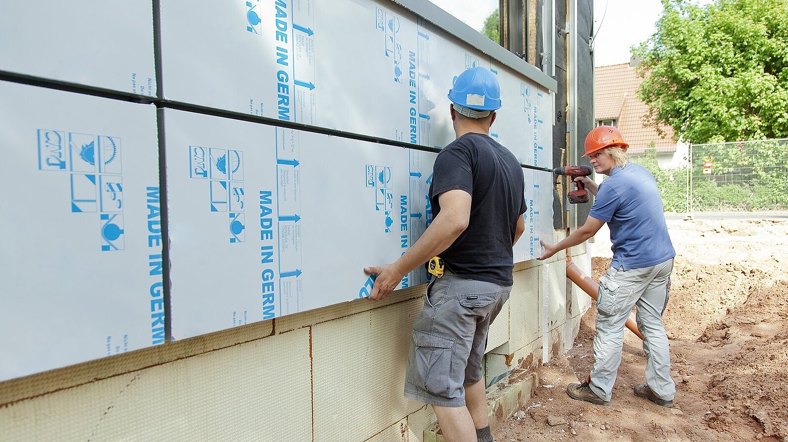 Zwei Männer montieren Verbundplatten zur Dämmung und Verkleidung einer Fassade.
