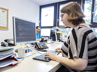 Eine junge Frau schreibt in Programmiersprache an einem Computer.