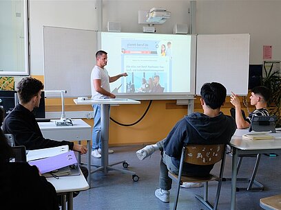 Ein Lehrer zeigt seiner Klasse planet-beruf.de auf einem Whiteboard.