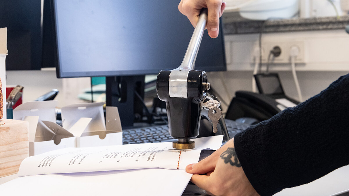 Auf einem Schreibtisch setzt jemand ein Stempelgerät auf ein Dokument.